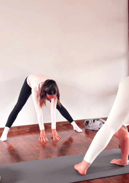 Two people practicing a forward fold yoga pose in a studio