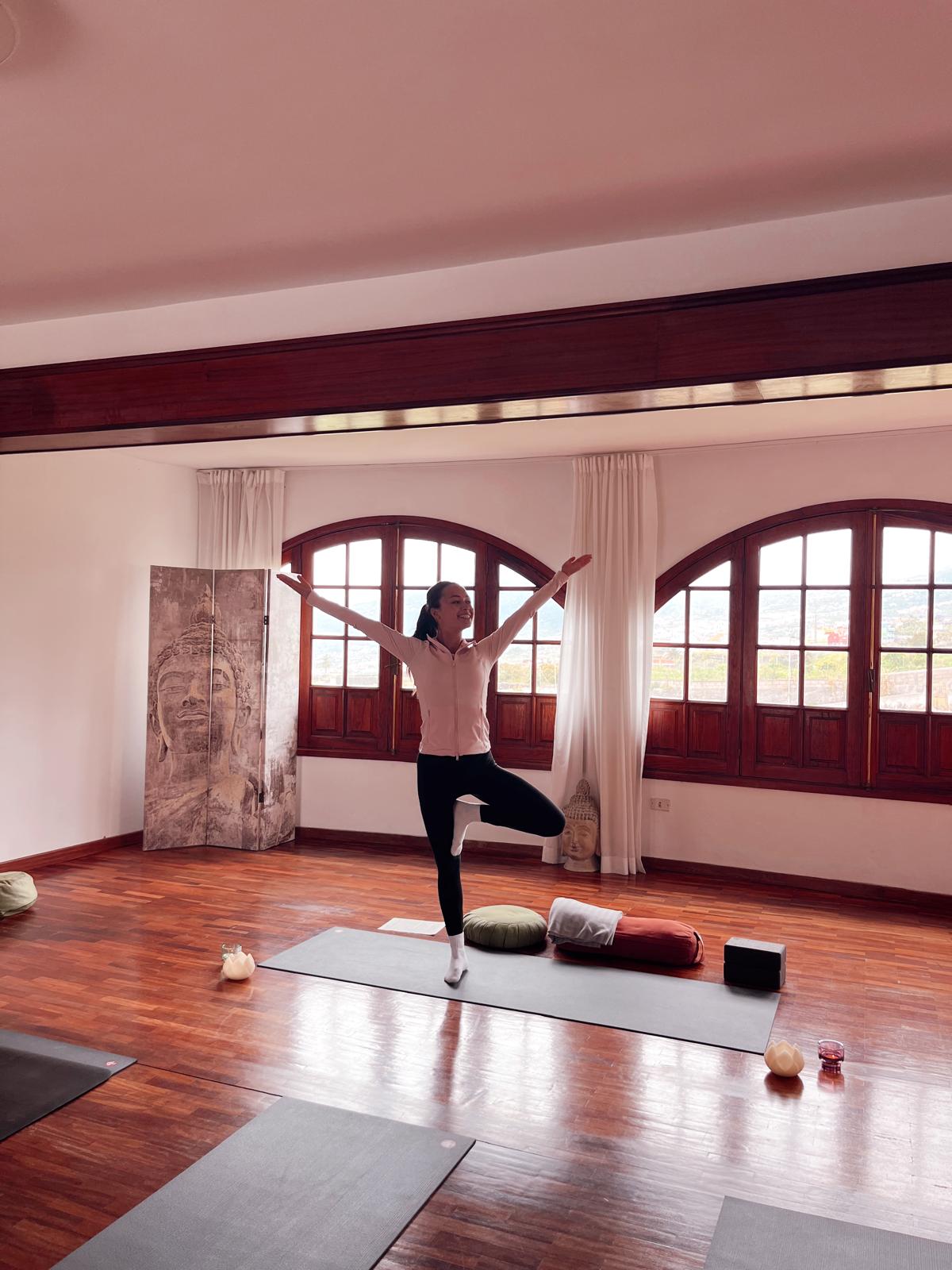 Jane smiling in a joyful tree pose in a sunlit yoga studio